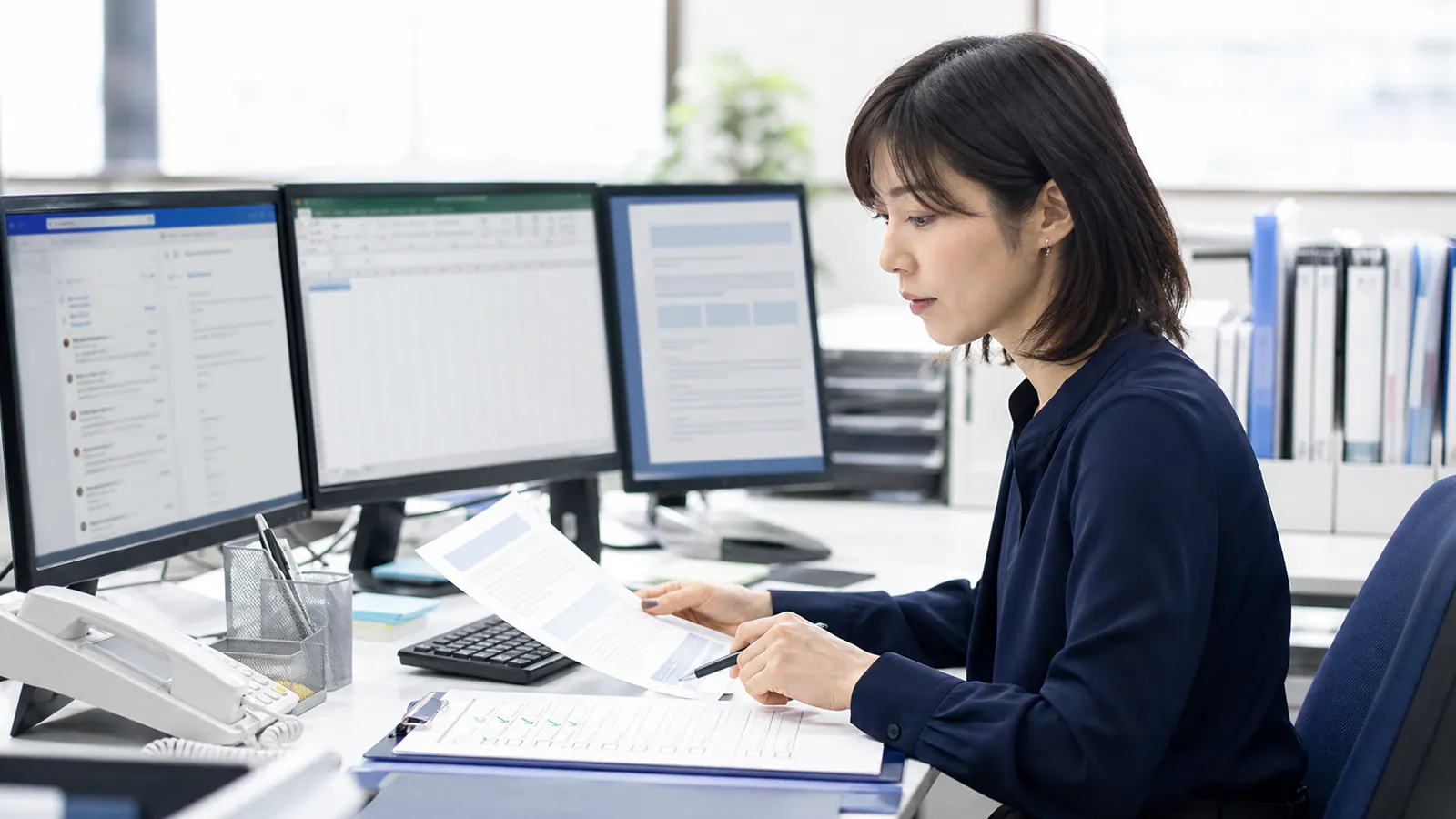 メール、表計算、確認表を見比べながらAIの下書きを検算する事務担当者